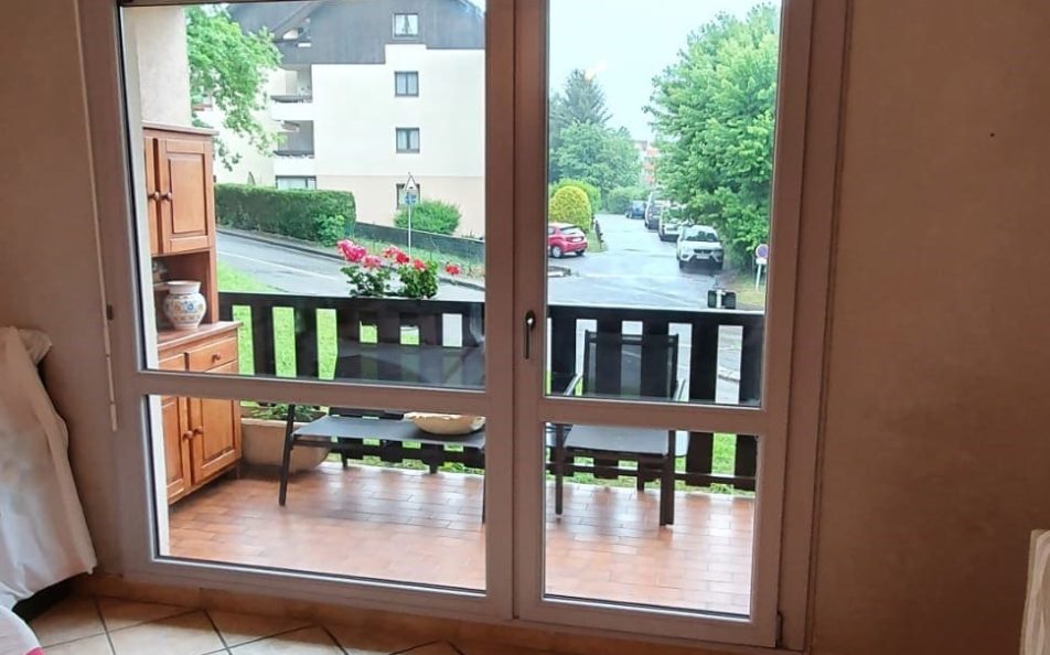 Vue intérieure salon carrelé sur baie et porte vitrée donnant sur une terrasse couverte